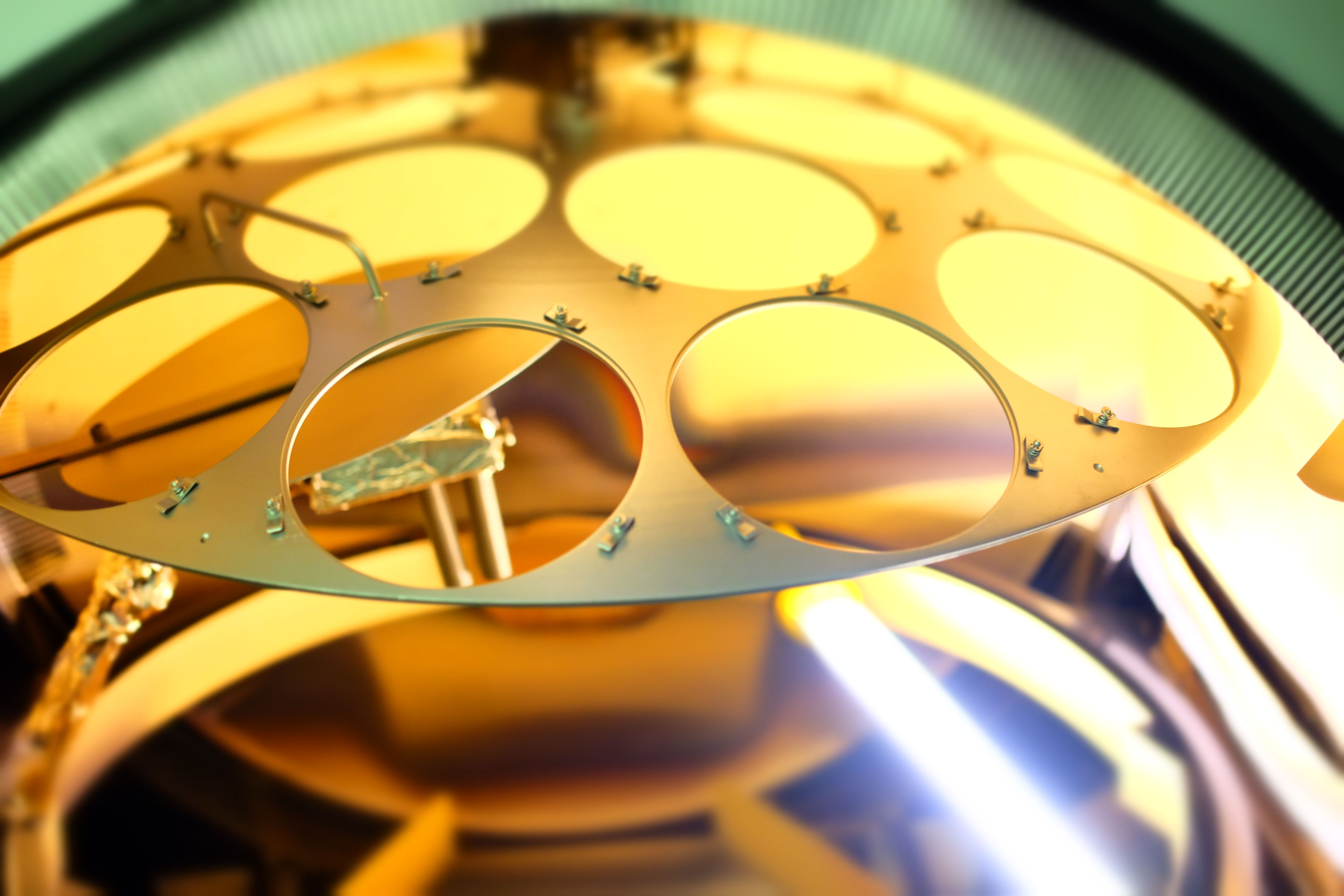 A photo of the inside of a metal evaporation chamber showing a semicircular tray with circular cutouts.