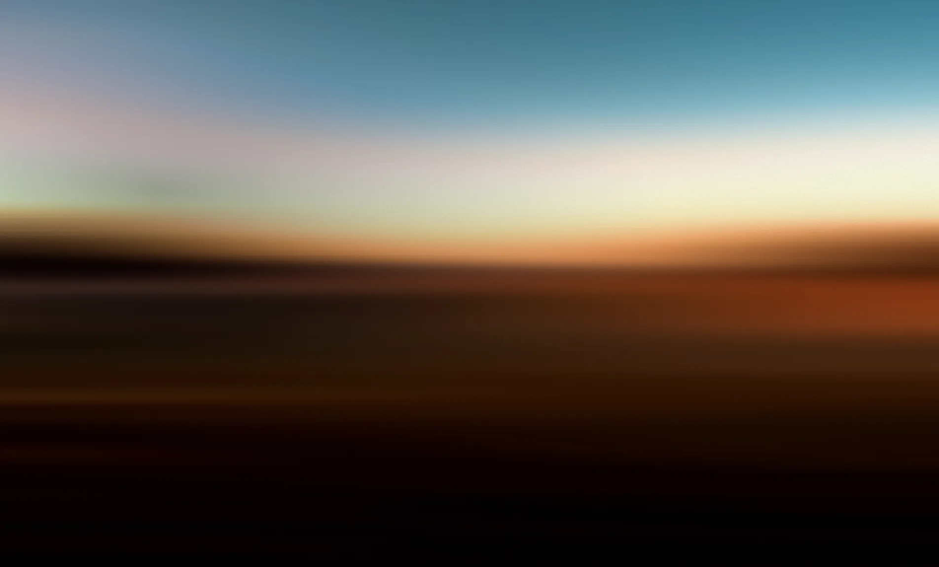 Abstract blurred horizon with gradient sky transitioning from blue through warm amber and orange tones to dark earth below.